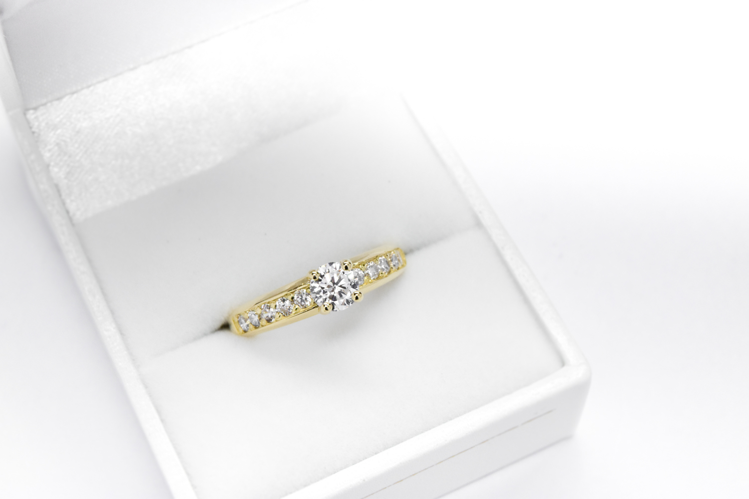 Anillo de compromiso de oro 18k amarillo con diamante blanco sobre un estuche blanco y fondo blanco