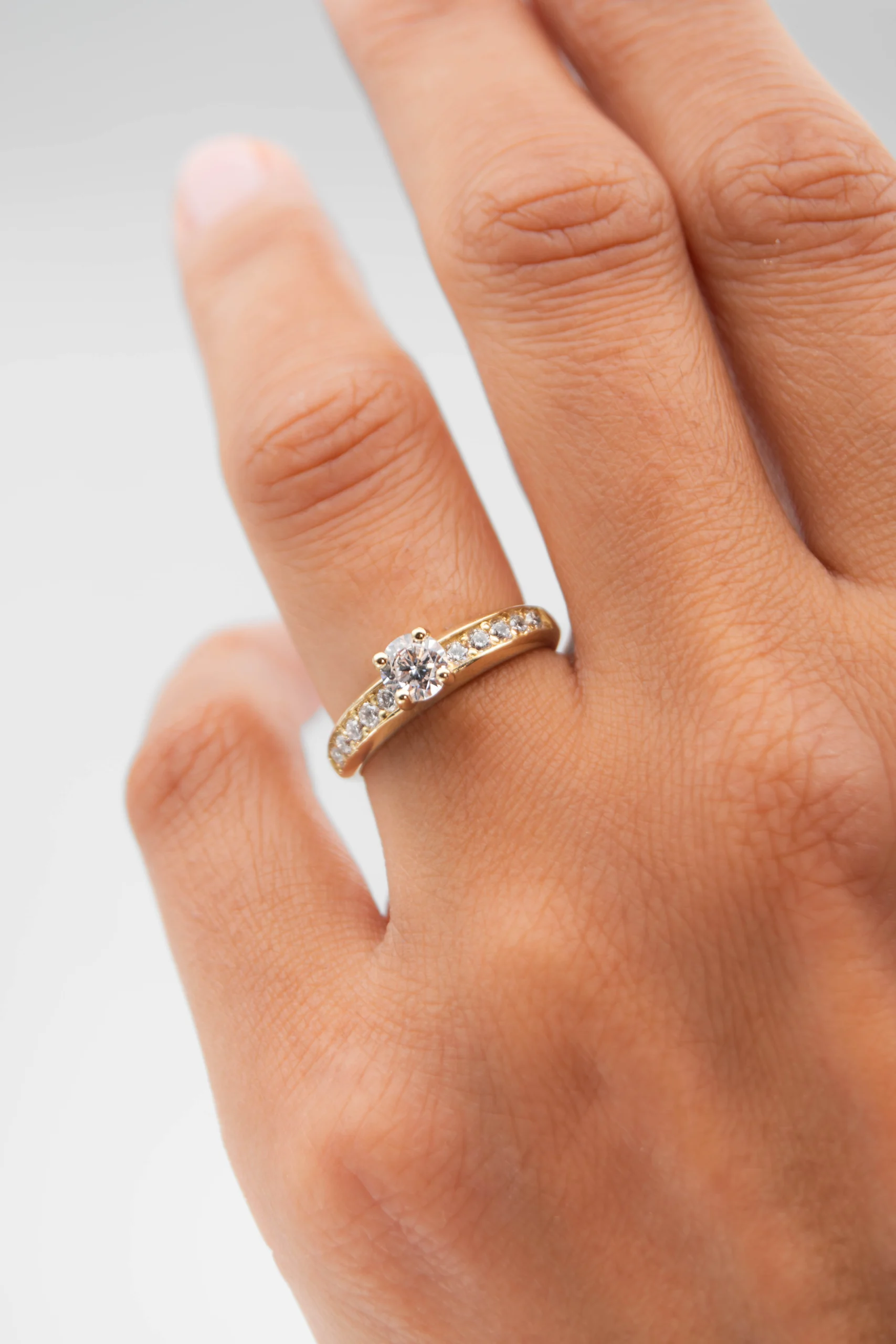 Anillo de compromiso de oro amarillo con un diamante natural en la mano de la modelo sobre fondo blanco