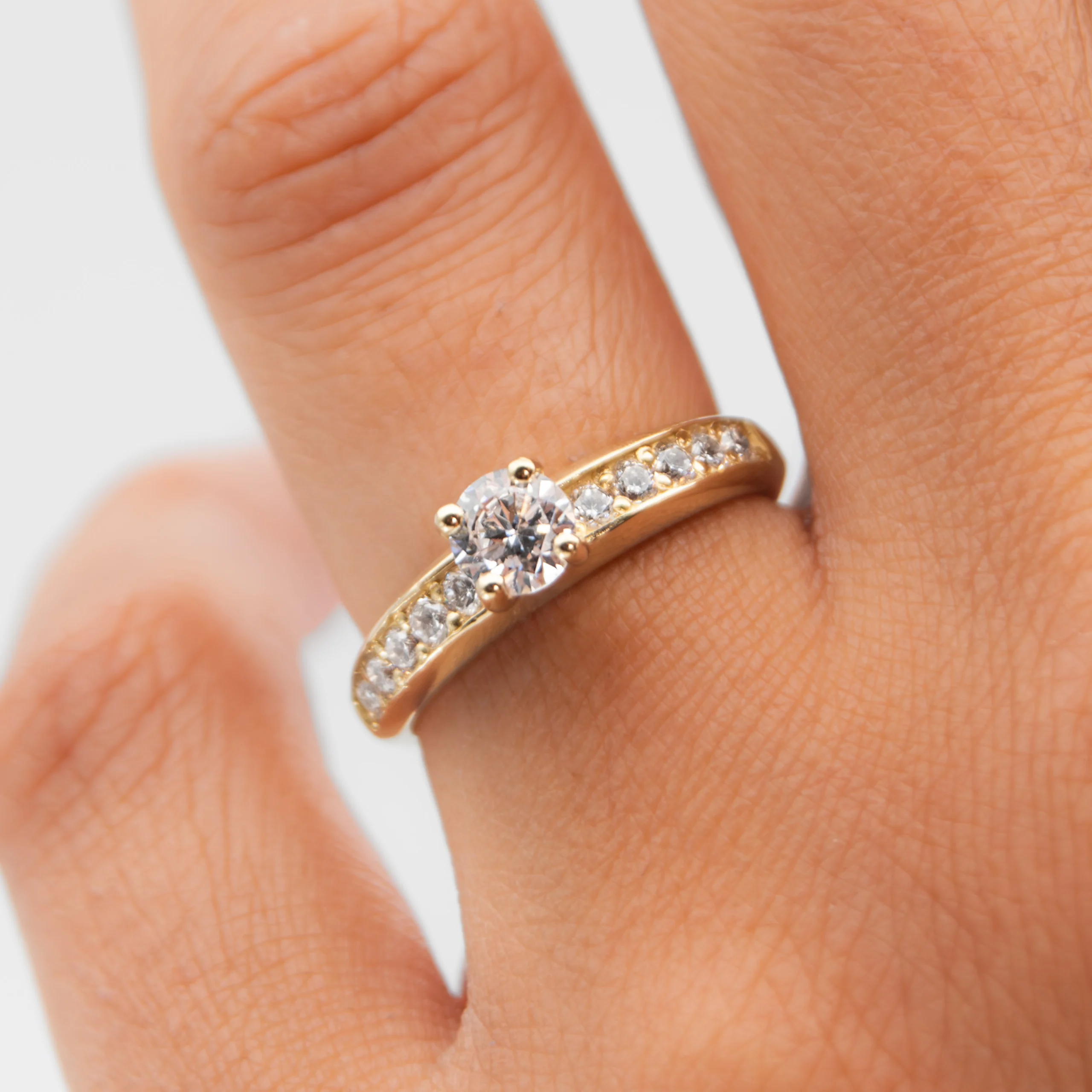 Anillo de compromiso de oro amarillo con un diamante natural en la mano de la modelo sobre fondo blanco
