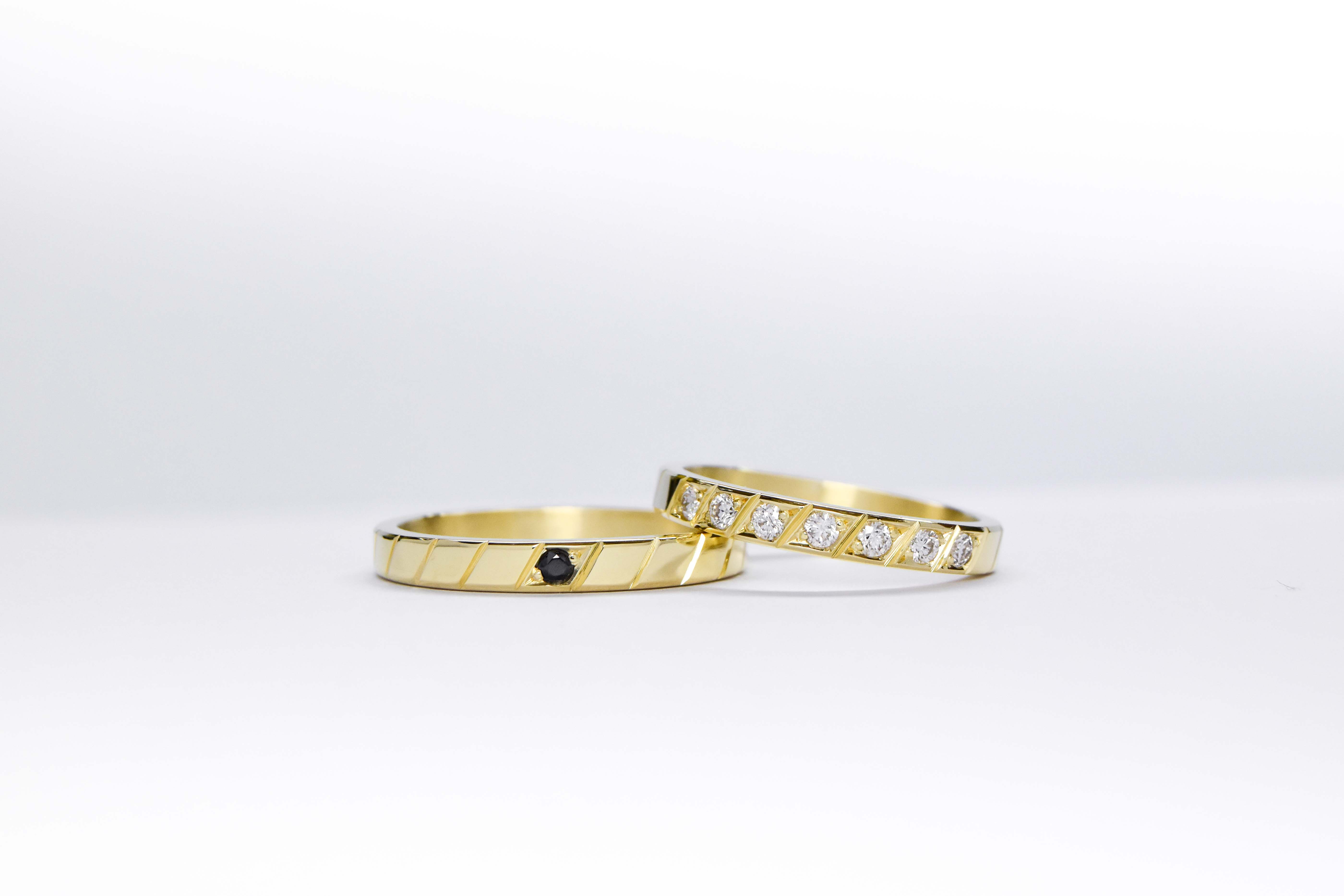 Alianzas de oro 18k amarillo con diamantes blancos engarzadas y gema negra a mano sobre fondo blanco