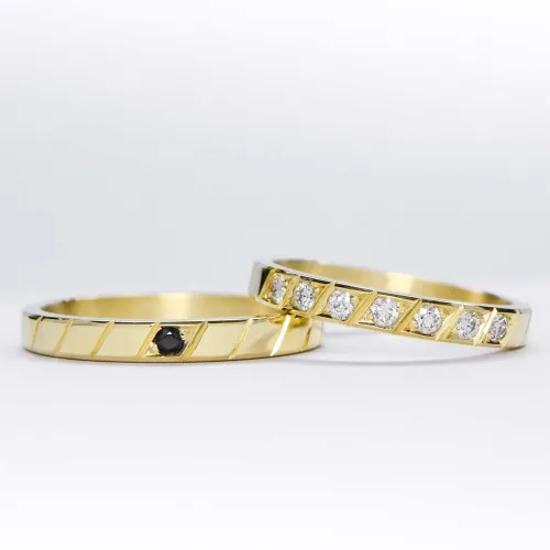 Alianzas de oro 18k amarillo con diamantes blancos engarzadas y gema negra a mano sobre fondo blanco