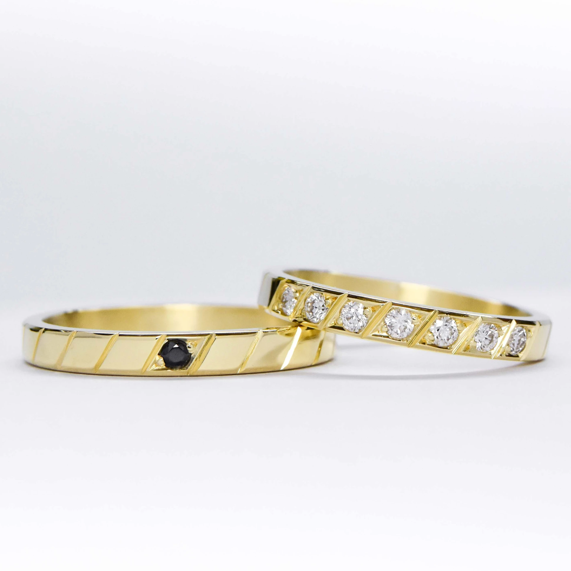 Alianzas de oro 18k amarillo con diamantes blancos engarzadas y gema negra a mano sobre fondo blanco
