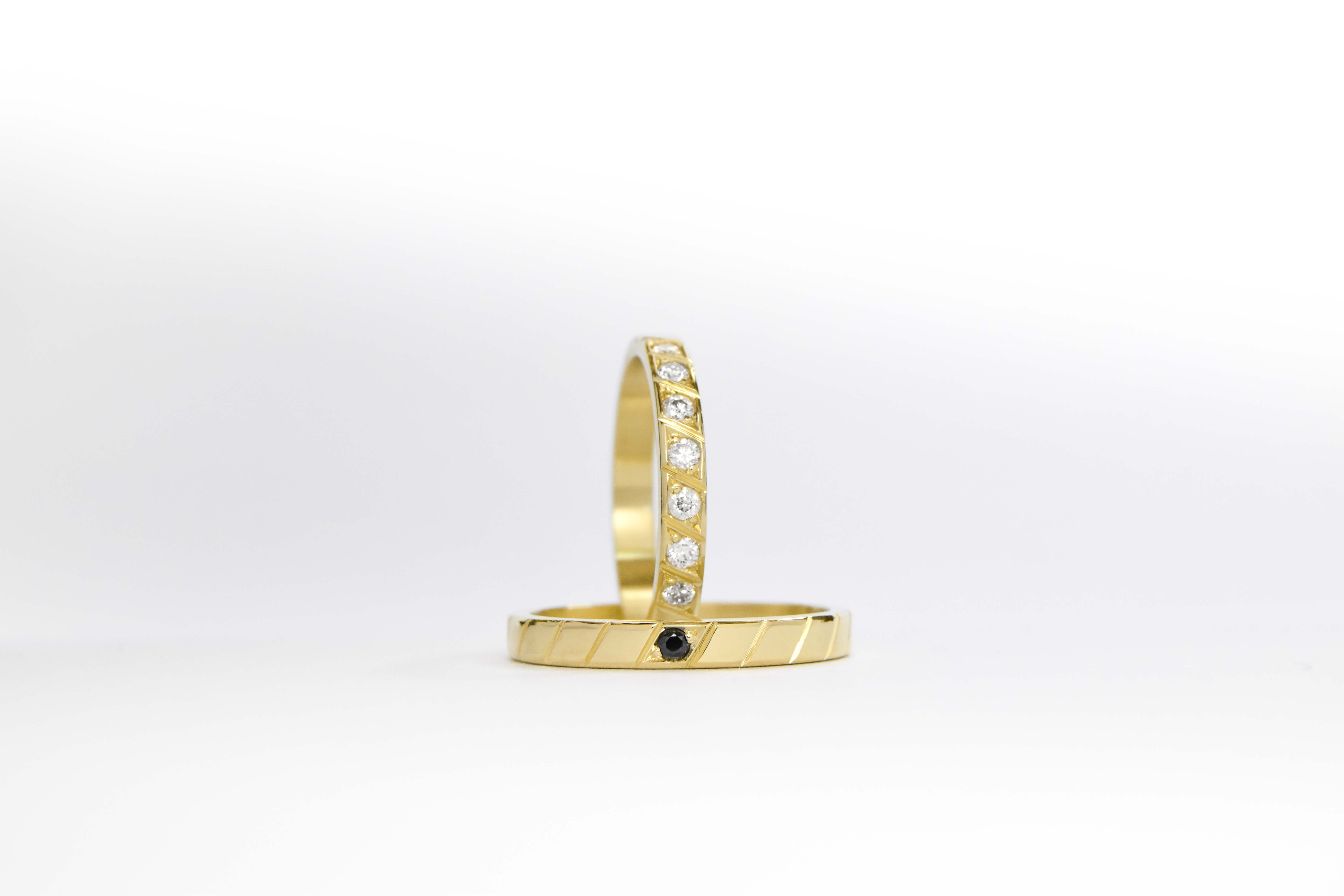 Alianzas de oro 18k amarillo con diamantes blancos engarzadas y gema negra a mano sobre fondo blanco