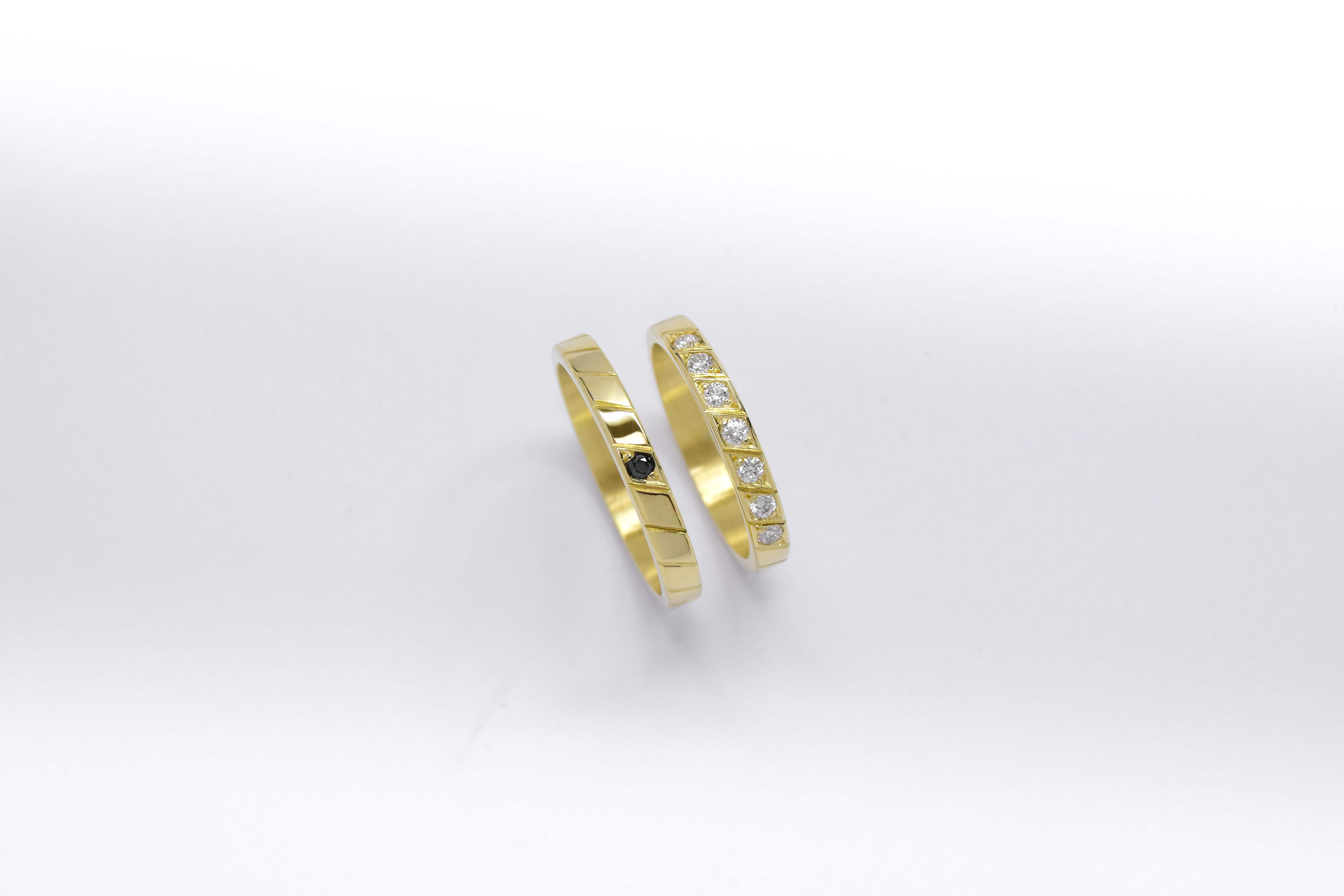 Alianzas de oro 18k amarillo con diamantes blancos engarzadas y gema negra a mano sobre fondo blanco