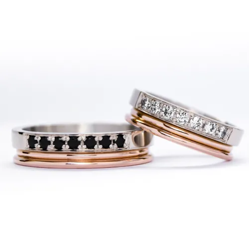 Alianzas de oro 18k rosa y blanco con gemas engarzadas en ambos anillos, diamantes blancos en el anillo de la mujer y gemas negras en el anillo del hombre. sobre fondo blanco.