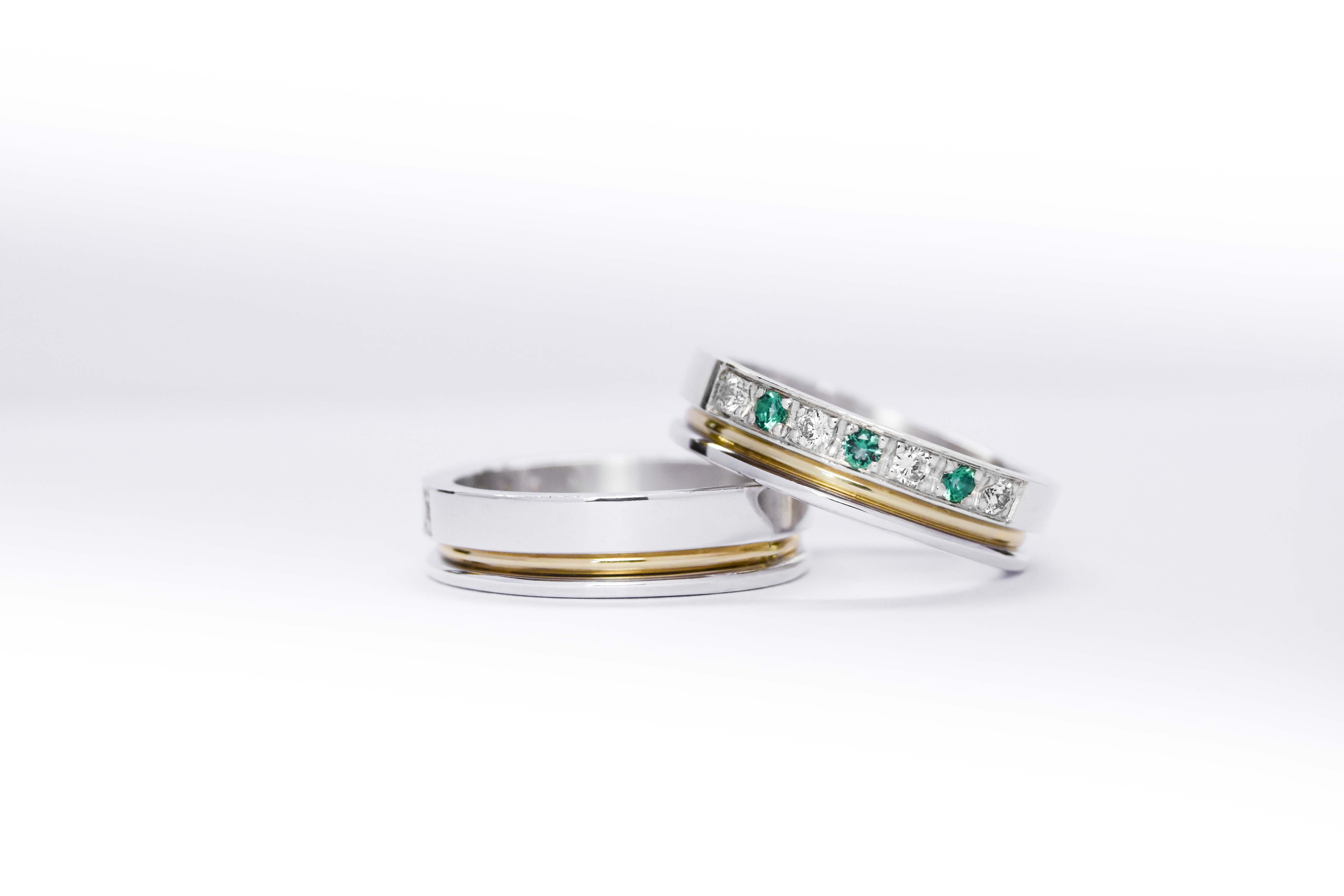 Alianzas de plata 950k y oro 18k amarillo con diamantes blancos y esmeraldas engarzadas. sobre fondo blanco.