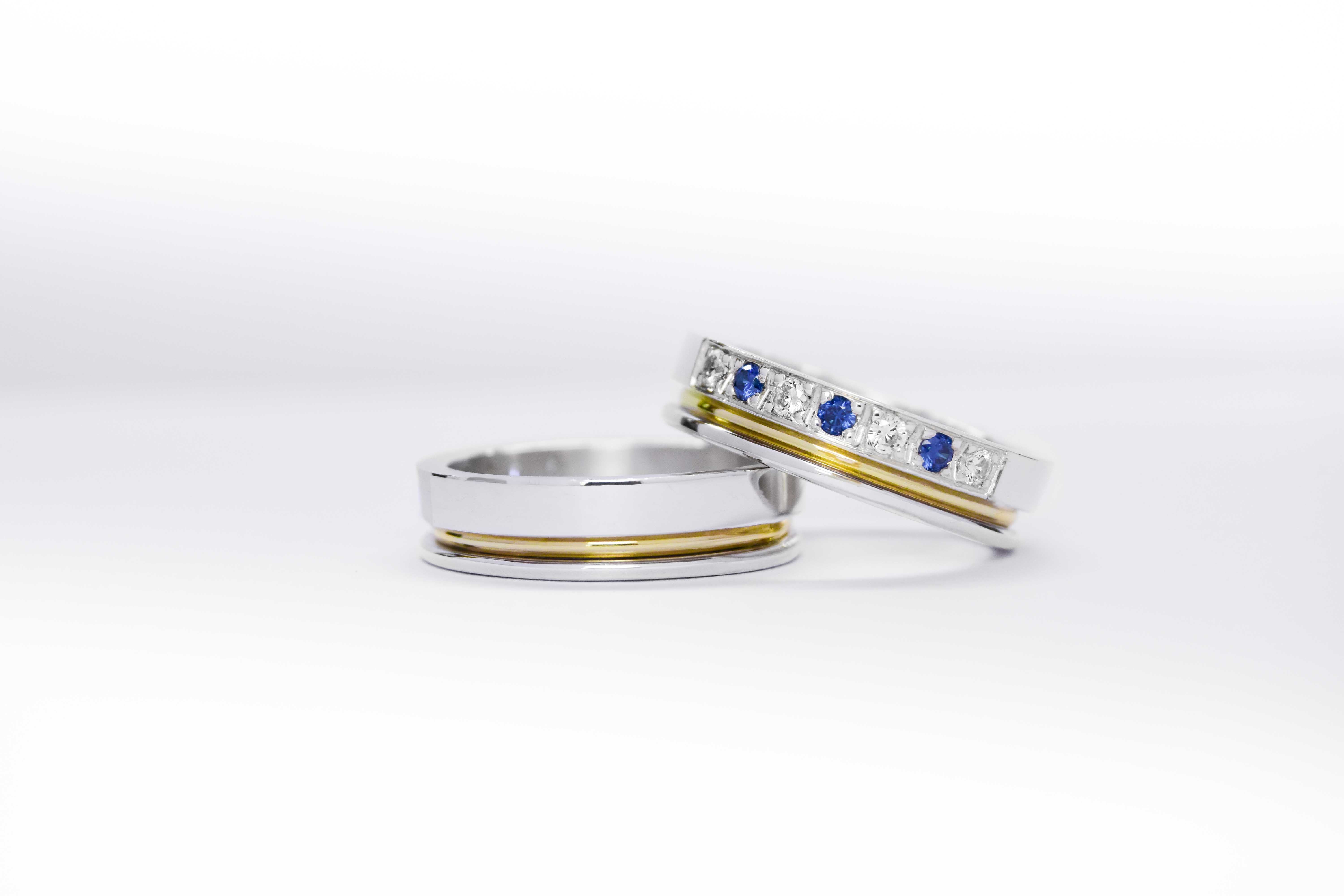 Alianzas de plata 950k y oro 18k amarillo con diamantes blancos y zafiros engarzadas. sobre fondo blanco.
