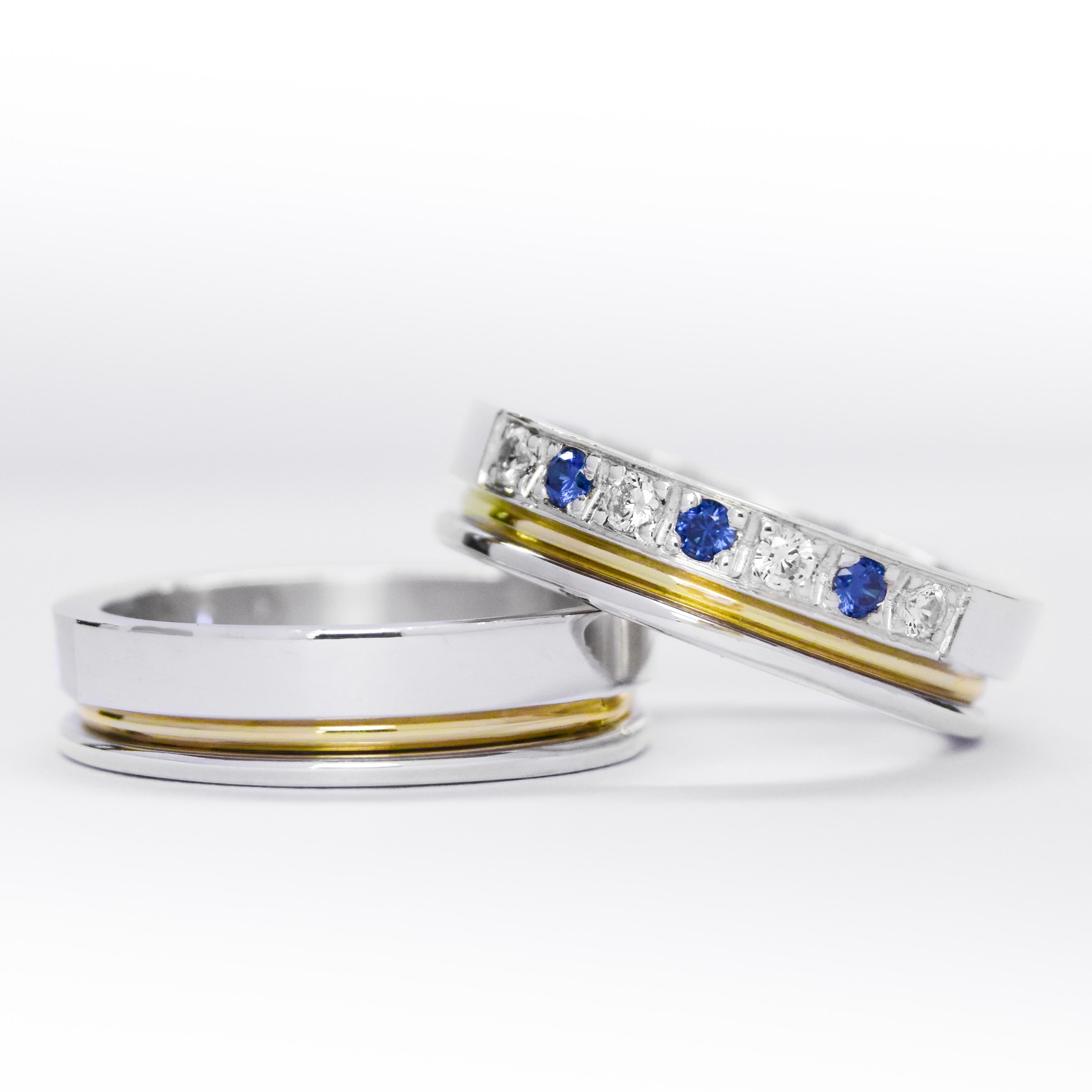 Alianzas de plata 950k y oro 18k amarillo con diamantes blancos y zafiros engarzadas. sobre fondo blanco.