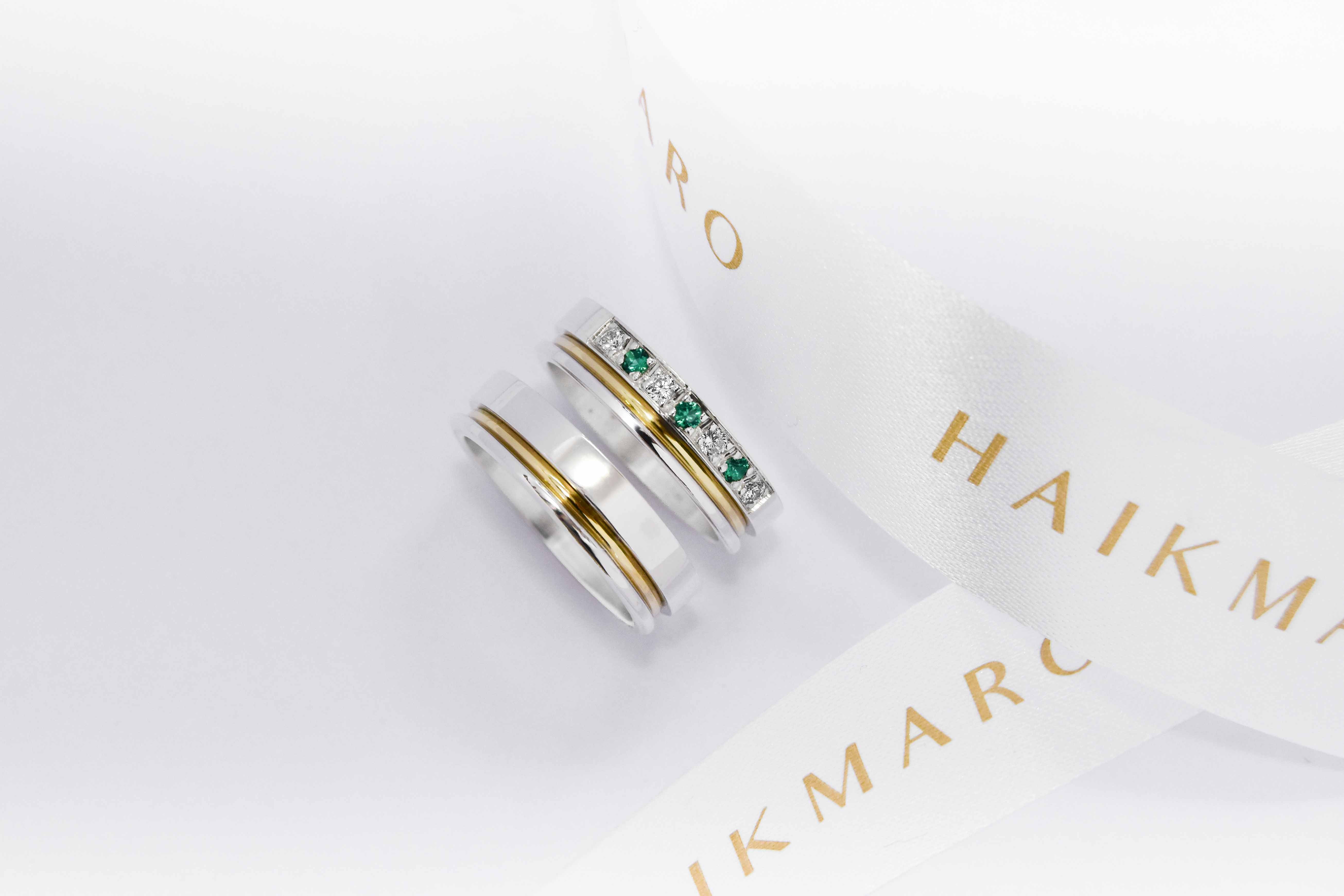 Alianzas de plata 950k y oro 18k amarillo con diamantes blancos y esmeraldas engarzadas. sobre fondo blanco.