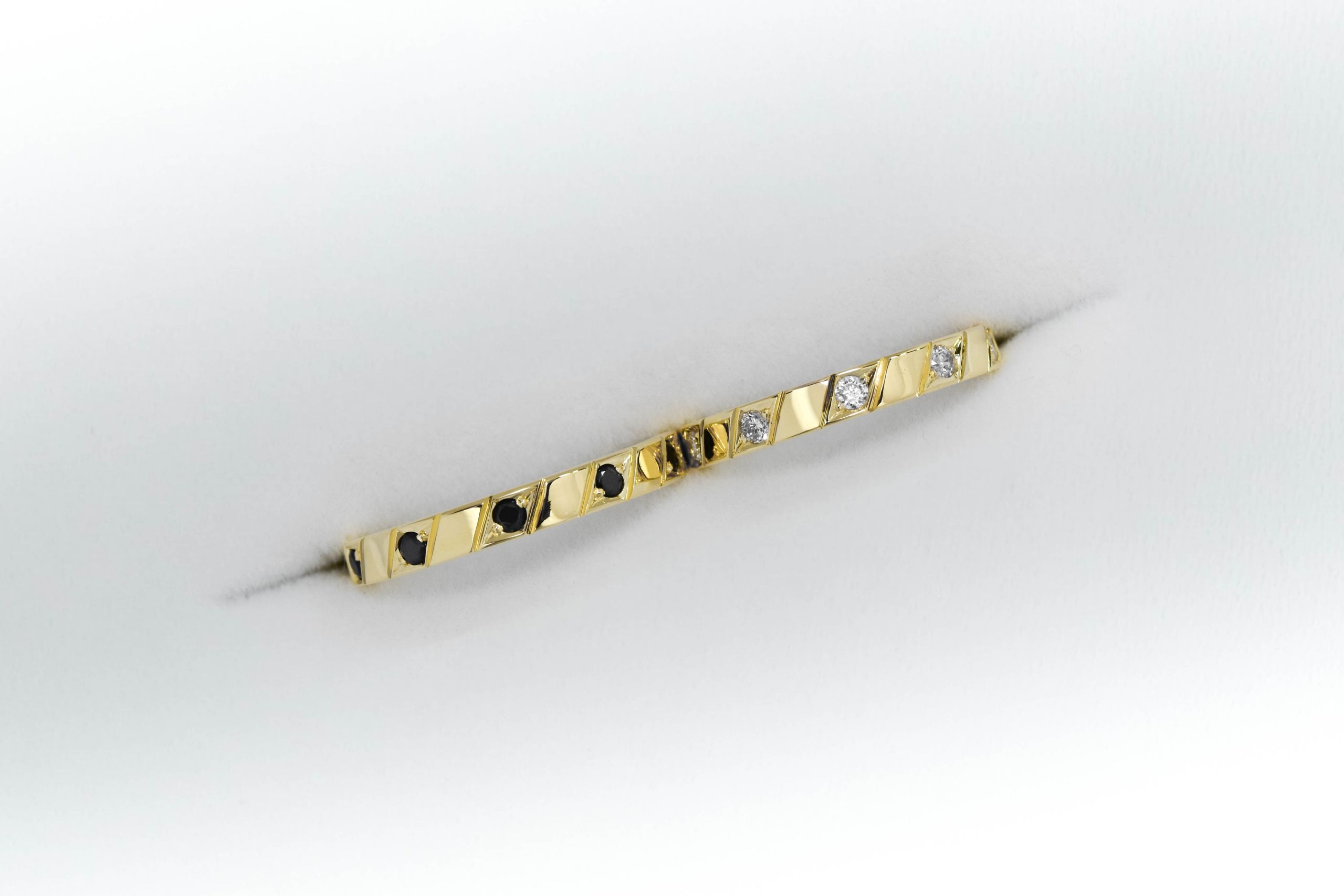 Alianzas de oro amarillo con 5 gemas blancas engarzadas en el anillo de la mujer y una gema negra engarzada en el anillo del hombre sobre fondo blanco.