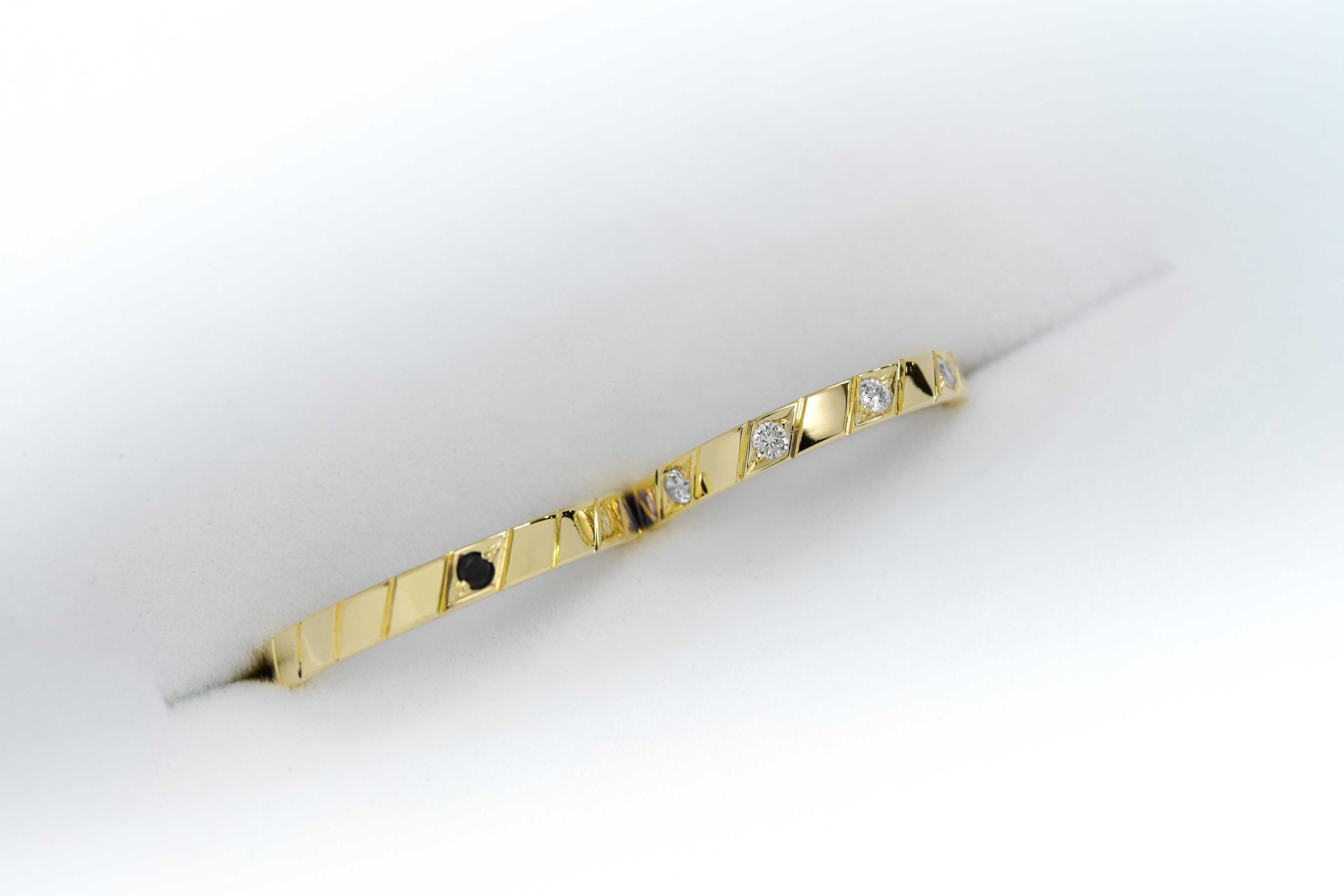 Alianzas de oro amarillo con 5 gemas blancas engarzadas en el anillo de la mujer y una gema negra engarzada en el anillo del hombre sobre fondo blanco.
