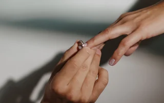 La manos del hombre sostiene un anillo de compromiso se lo esta colocando en el dedo de la mujer.