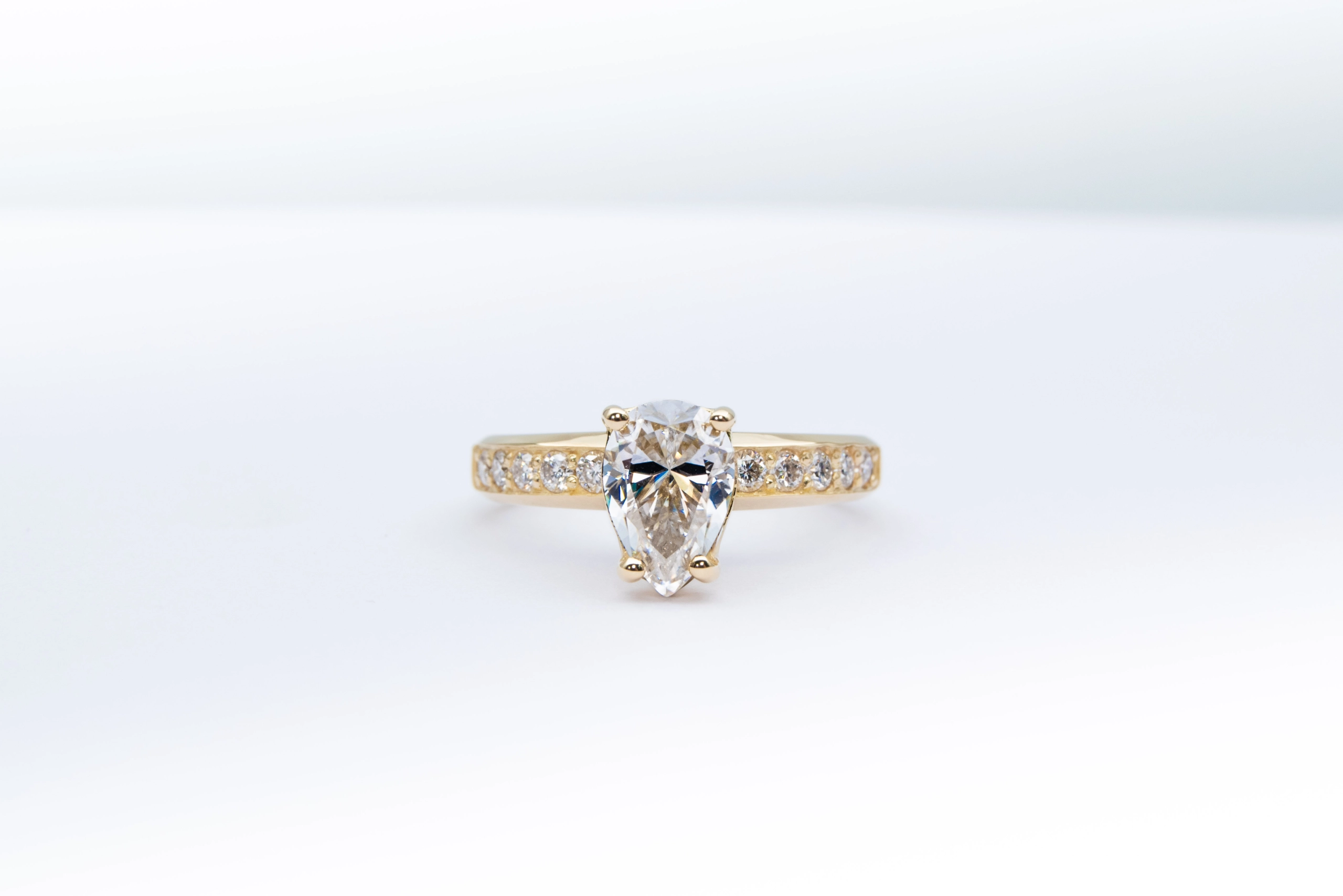 anillo de compromiso de oro modelo Taylor más con gema pear cut sobre fondo blanco