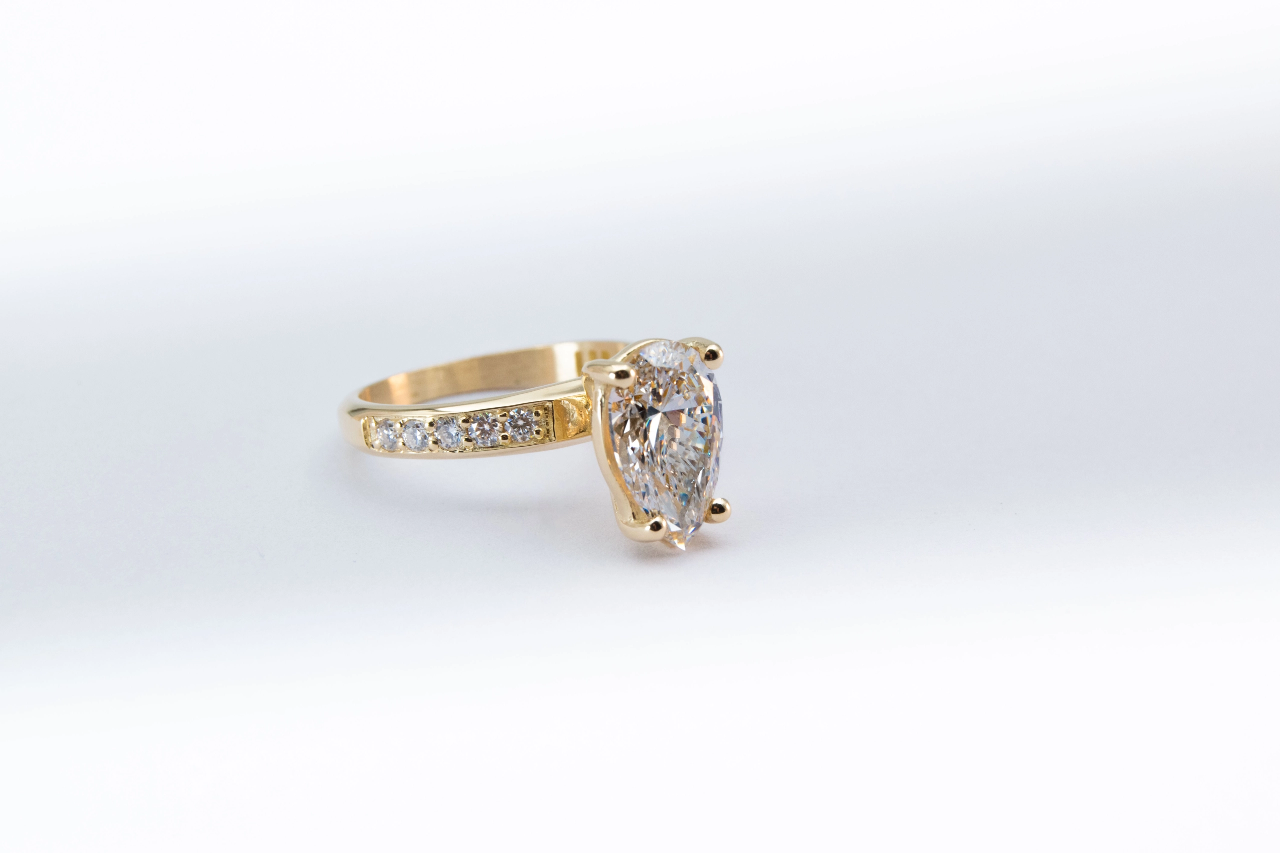 anillo de compromiso de oro modelo Taylor más con gema pear cut sobre fondo blanco
