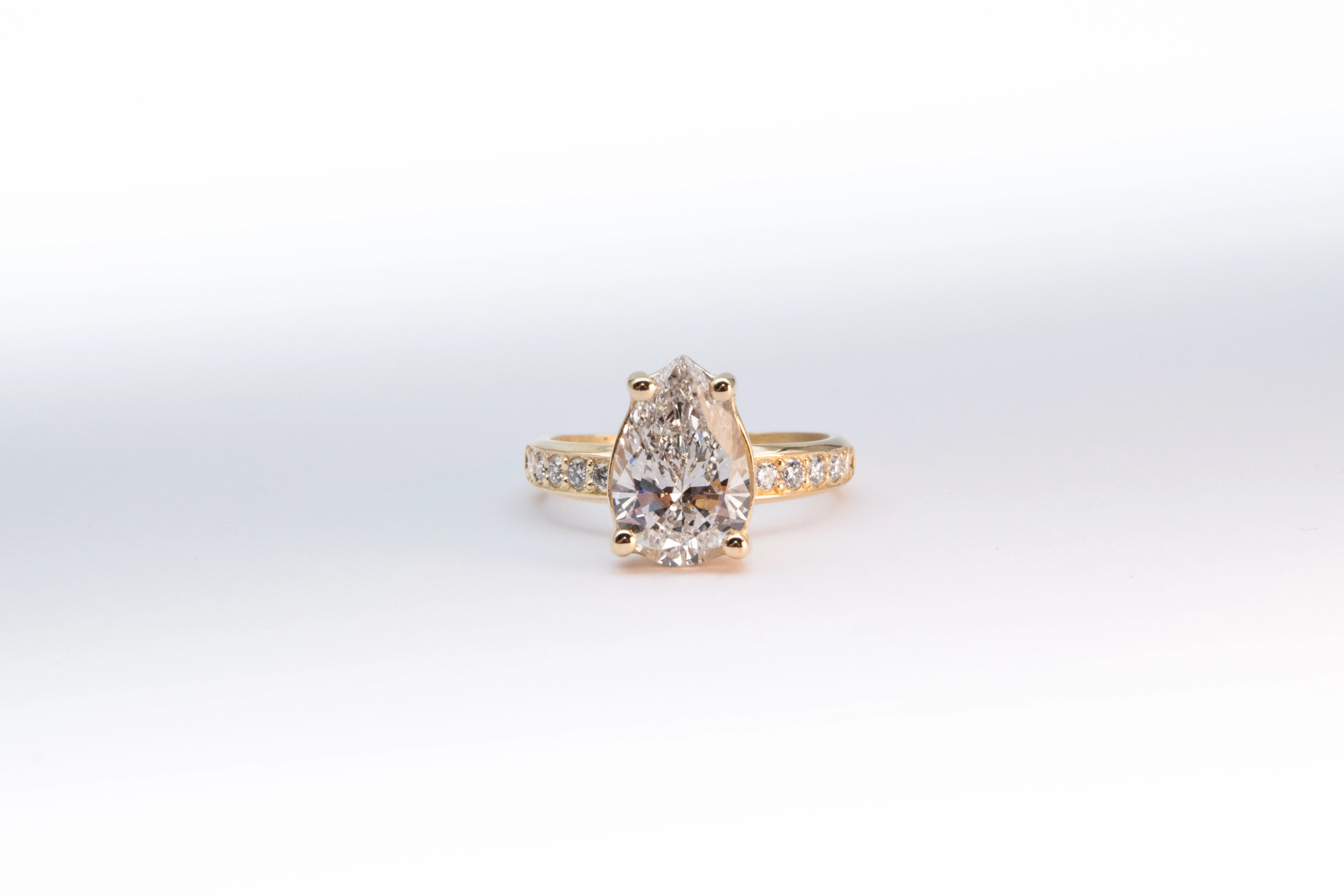 anillo de compromiso de oro modelo Taylor más con gema pear cut sobre fondo blanco