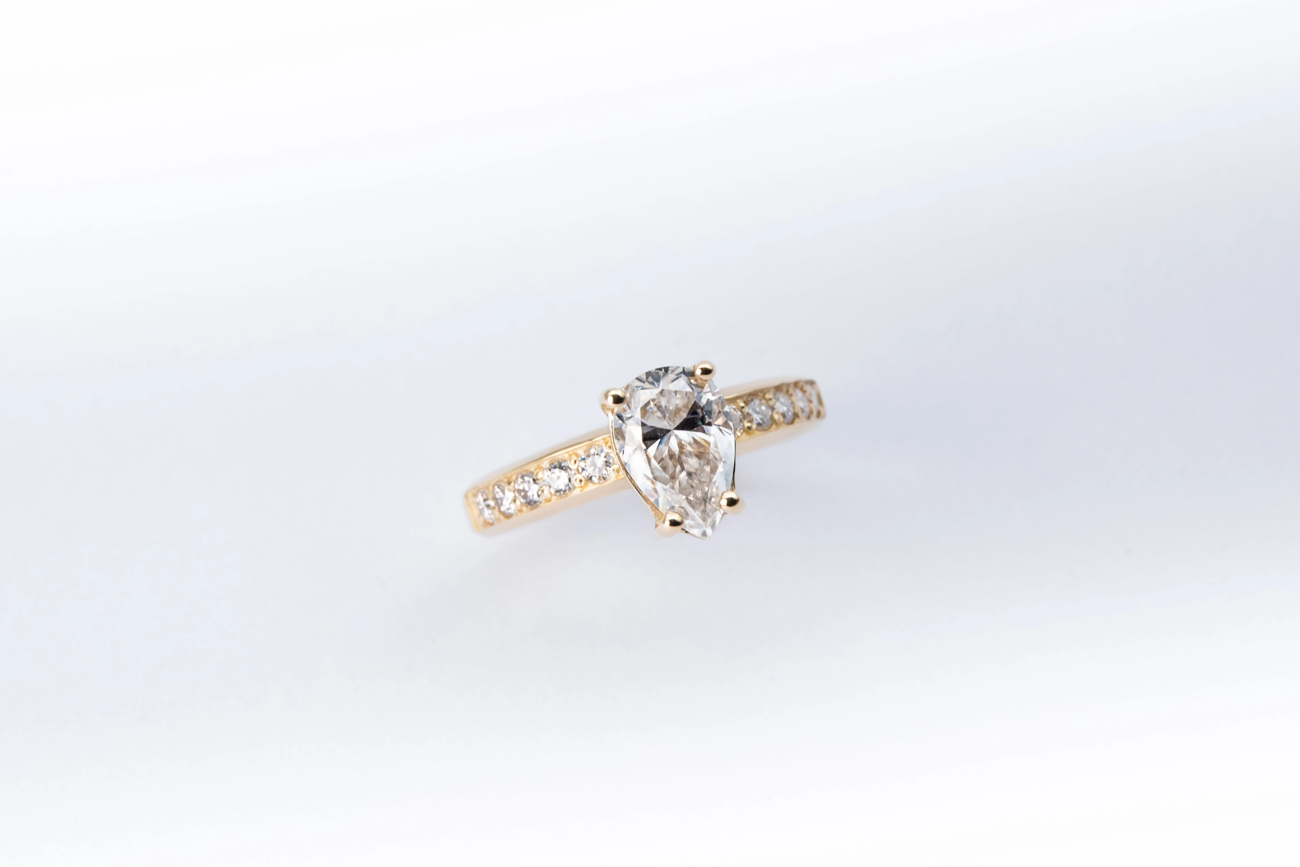 anillo de compromiso de oro modelo Taylor más con gema pear cut sobre fondo blanco