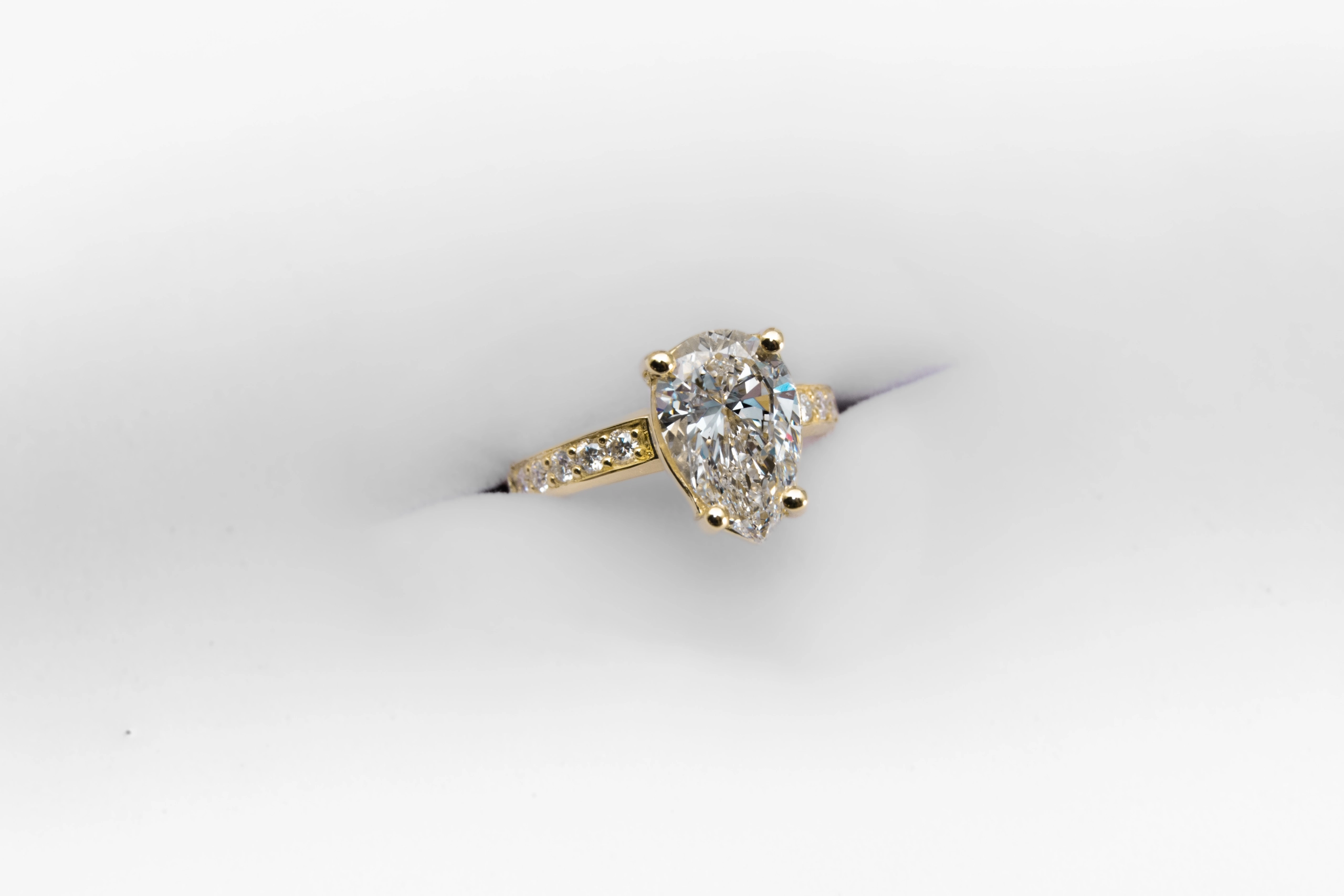 anillo de compromiso de oro modelo Taylor más con gema pear cut sobre fondo blanco