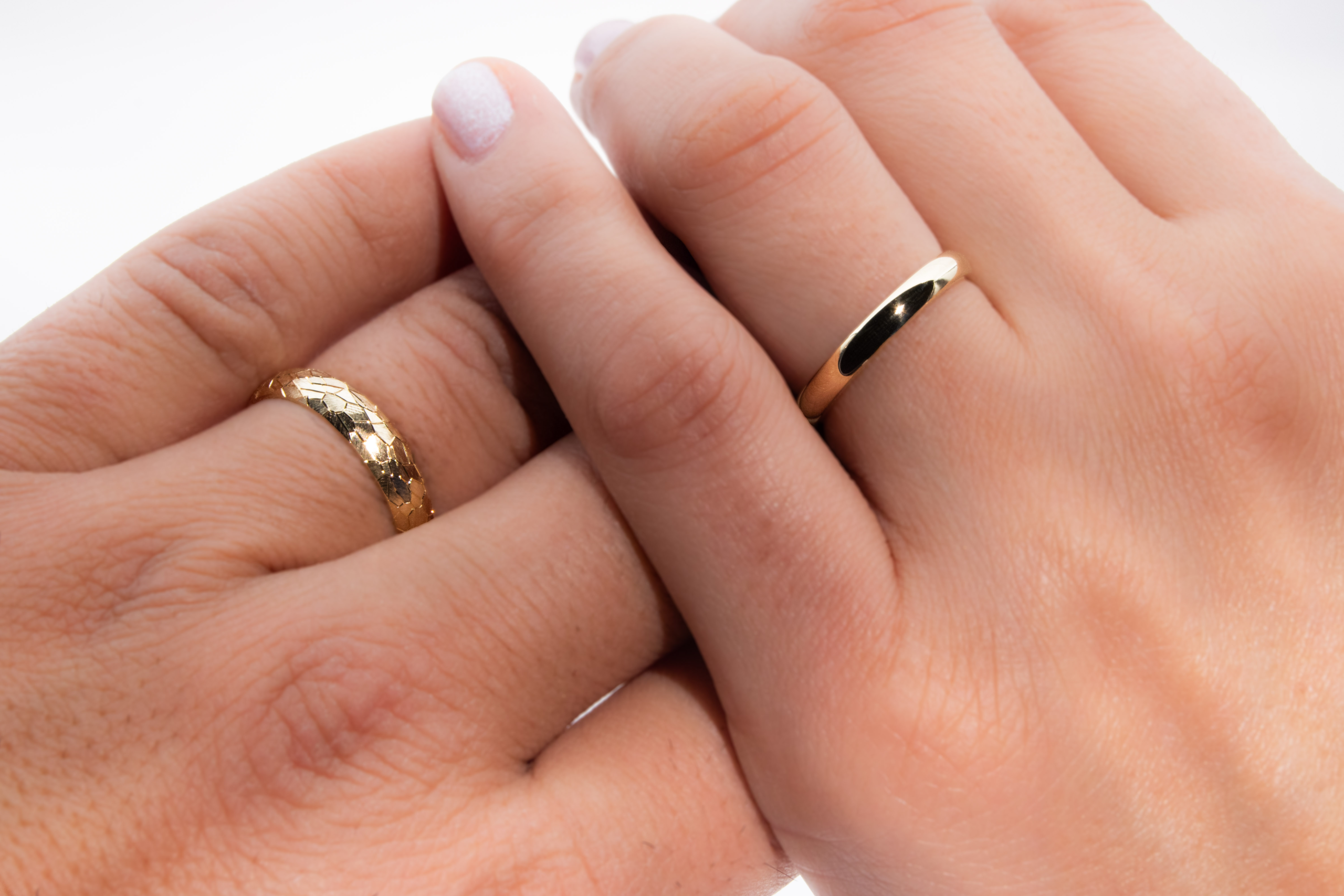Alianzas de casamiento de oro 18K con textura de diferentes anchos modelo Perseo sobre las manos de los modelos